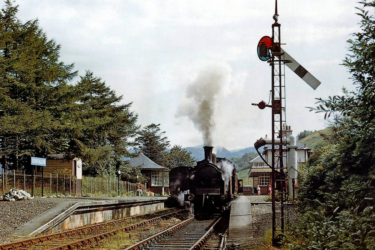 A steam train arriving at Kentallen Station, with the signal box and station house behind